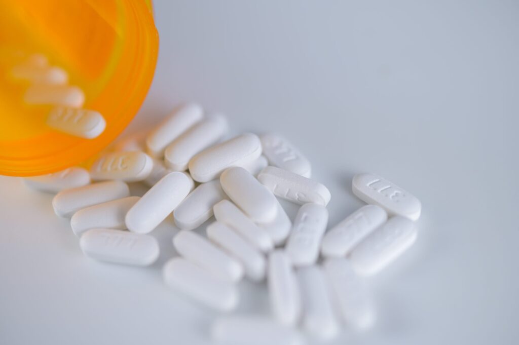An orange prescription pill bottle tipped over with several white oblong tablets scattered on a white surface.