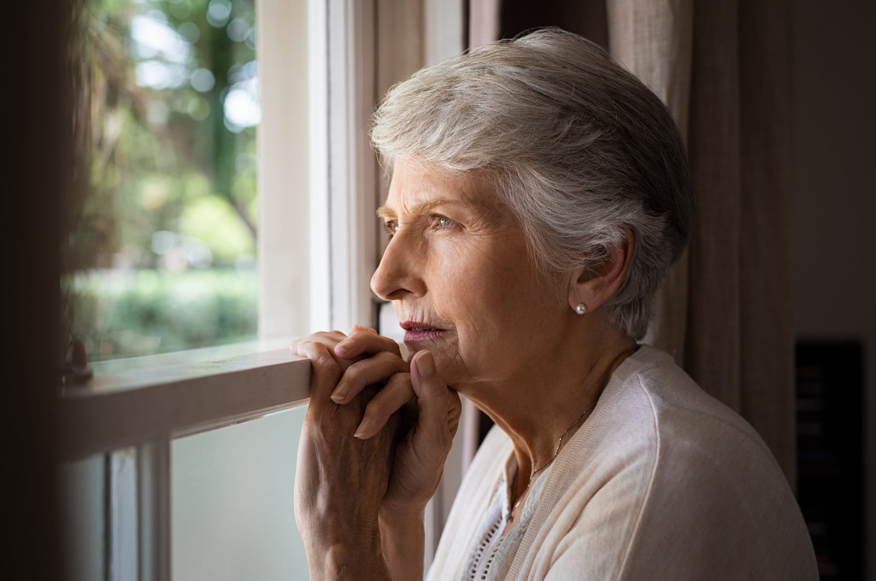 Older woman looking sadly out a window
