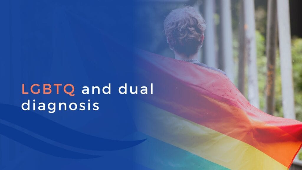 A person with short hair stands outdoors, draped in a rainbow pride flag. Beside them, blue text reads LGBTQIA+ and dual diagnosis on a blue background.