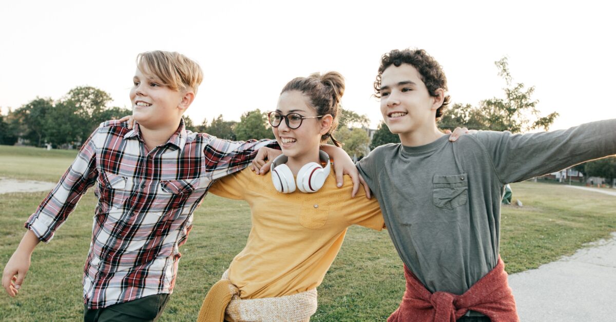 A group of teenagers walk arm in arm on a concrete path outside. Positive peer networks are a powerful way to prevent drug addiction later in life.