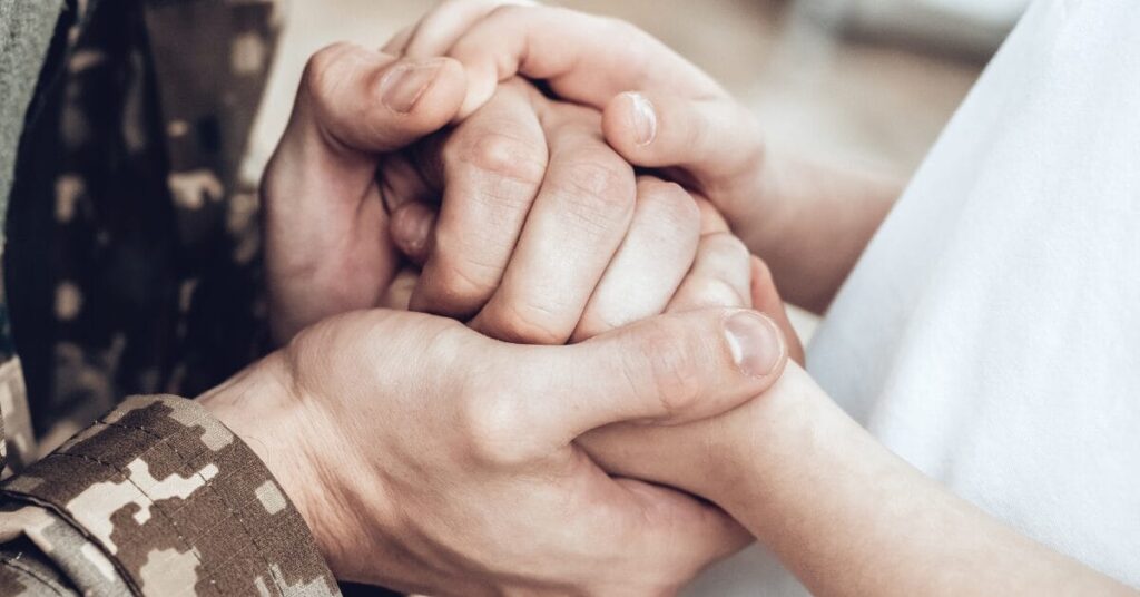 A person wearing a military uniform clasps hands with a different person in a white T-shirt, representing Purple Heart Day.