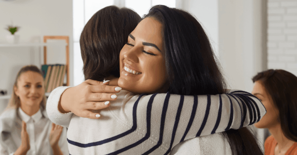 Two women embrace in a group therapy session. Therapy is key to addiction treatment and can be helpful for suicide prevention as well.