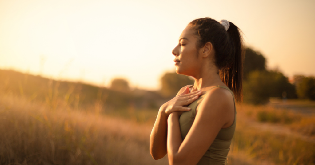 An image of a woman, hands to her heart in the sunset, emphasizing self-love and addiction on Valentine's Day.