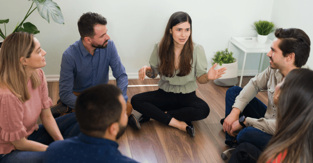 Group therapy discussion of men and women sitting on the floor discussing national counseling awareness and why it's important .